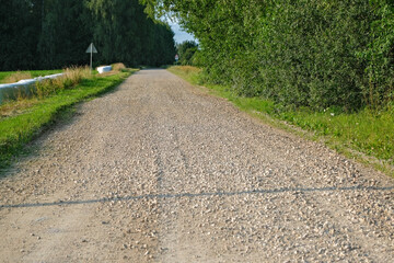 gravel road in Latvia countryside in summer. Cattle food bales on road side