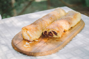 Freshly Baked Cherry Strudel on Rustic Wooden Cutting Board Outdoors in Sunlit Garden Ambiance...