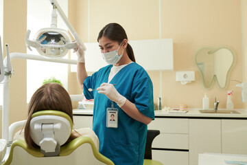 Young adult woman dentist examining teeth of Caucasian child patient in dental clinic, holding...