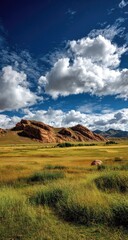 Fototapeta premium Vast grassland stretches beneath a vibrant sky filled with puffy clouds, dramatic reddish-brown hills rise in the background