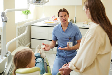 Caucasian male dentist explaining dental procedure to Caucasian teenage girl sitting in dental...