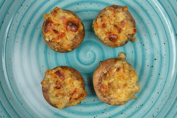 A top-down view of four baked stuffed mushrooms with melted cheese on a blue plate