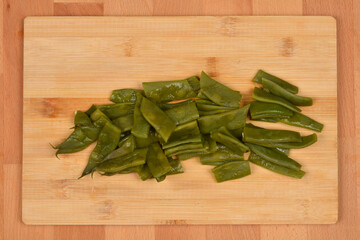 Sliced, cooked green beans are shown on a wooden cutting board, photographed from above