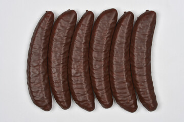 A close-up, top-down view of six dark chocolate-covered banana-shaped candies arranged in a row on a light background