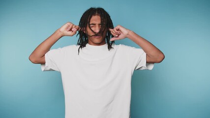 footage of young man appears stressed and overwhelmed while covering his ears with fingers on light blue background