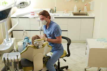 Caucasian male dentist examining teeth of Caucasian child patient in dental clinic, dentist wearing...