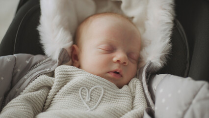 Newborn baby sleeping peacefully in car seat wearing winter clothes