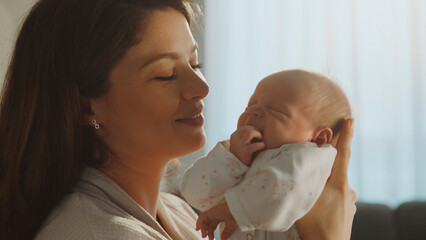 Loving mother holding her adorable newborn baby at home