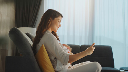Happy mother breastfeeding newborn baby and using smartphone at home