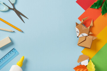 Origami deer, mushroom and leaves with colorful paper and craft supplies on a blue background Handmade art and creativity. Copyspace