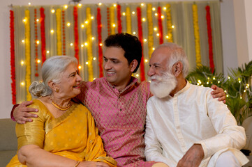 Indian happy family looking each other in traditional wear sitting on sofa indoor with smile on the...