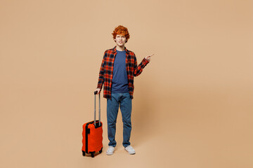 Traveler happy man wear casual clothes hold suitcase bag point aside isolated on plain pastel beige...