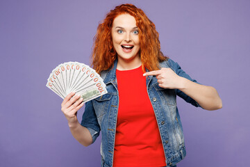 Young ginger woman wears red t-shirt denim shirt hold in hand point finger on fan of cash money in...