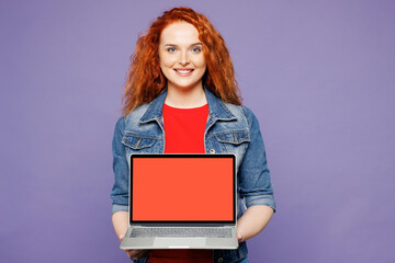 Young ginger IT woman she wears red t-shirt denim shirt hold use work on laptop pc computer with...
