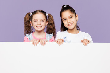 Little two friends kids children girls 9-10 years old wear casual clothes together hold big white poster billboard for promotional content, place for text or image isolated on plain purple background.