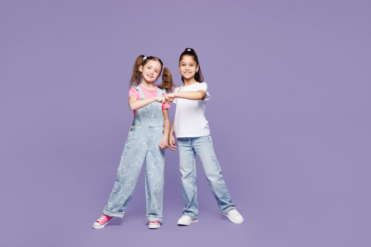 Full body little smiling happy fun two friends kids children girls 9-10 years old wear casual clothes together do fist bump gesture look camera isolated on plain purple background. Lifestyle concept.