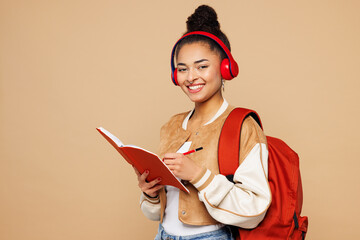 Young girl student wear casual clothes backpack bag hold books listen to music in headphones write...
