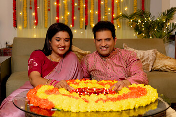 Beautiful indian happy couple decorating together a 
thali full of diyas with marigold rangoli on...