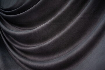 A close-up of dark, luxurious fabric with soft, flowing folds. The smooth texture and gentle drapes...