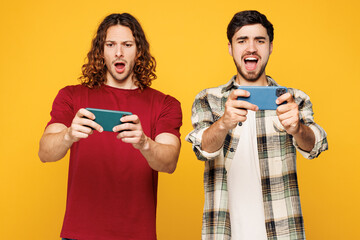 Young sad two friends buddies men wear casual clothes use play racing app on mobile cell phone hold...