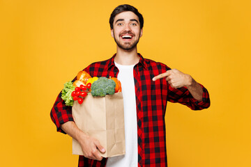 Young surprised man in casual clothes hold craft paper bag for takeaway point index finger on mock...