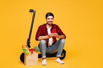 Full body young man wearing casual clothes hold paper bag for takeaway with food products sit on...