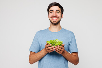 Young happy man he wears blue t-shirt casual clothes hold bunch of lettuce salad in bowl look...