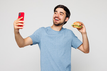 Young fun man he wear blue t-shirt casual clothes hold eat burger do selfie shot on mobile cell...
