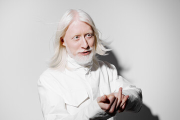 White haired man in a light colored outfit with flowing hair, against a plain white background depicting creativity and artistic expression His gesture invites curiosity and intrigue