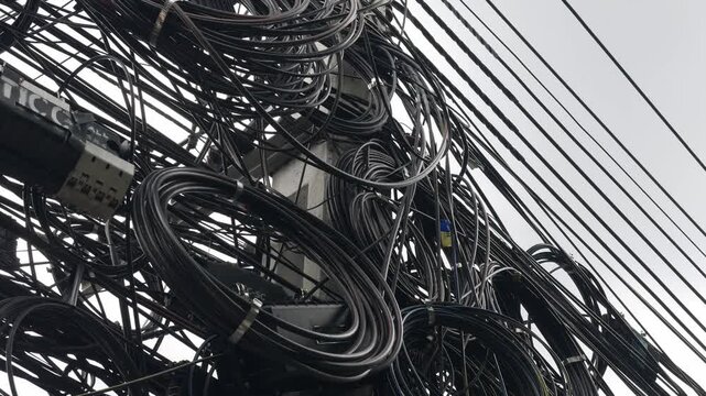 Messy tangled overhead cable wires on utility pole in urban city infrastructure.