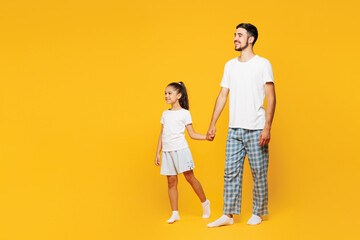 Full body young fun happy parent man with child girl wear casual blue pyjamas clothes. Daddy little kid daughter walk go hold hand isolated on plain yellow background Father's Day Love family concept