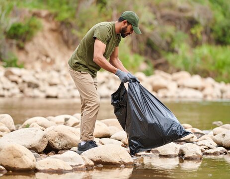 Man picking up trash from rocky river during environmental cleanup - Powered by Adobe