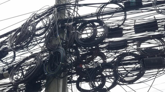 Messy tangled overhead cable wires on utility pole in urban city infrastructure.