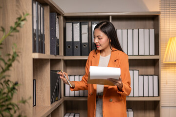 woman in an orange jacket is looking through a shelf of binders