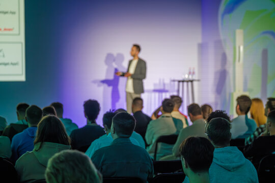 Professional speaker delivering presentation to audience in a modern conference setting with vibrant environment and engaging atmosphere