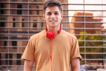 Portrait of a young man smiling warmly at the camera while wearing red headphones around his neck,...