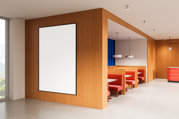 Vertical blank poster mockup on wooden wall in modern cafe interior with red booth seating and...