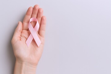 Naklejka premium Pink Ribbon Symbol Held in Hand: Breast Cancer Awareness, Hope, and Support on Gray Background
