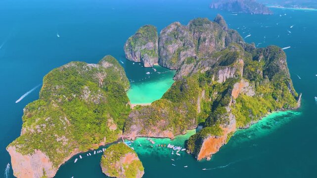 Aerial panoramic beautiful view of Phi phi island ring of steep limestone cliff hills surrounding Maya Bay white sand beaches coral reefs around, boats floating nearby