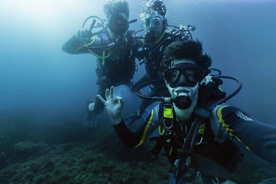Open Water Diving instructor with two friends doing advanced course, taking selfie under the sea, enjoying vacations adventure deep in the ocean