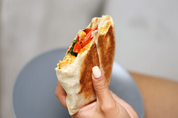 Hand holding grilled tortilla wrap. Fresh vegetables and chicken visible inside. Tasty street food...