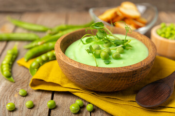 Green pea soup on a wooden table. Fresh pea soup bowl. Delicious healthy cream soup in a bowl with green peas and croutons. Healthy vegan puree. Copy space. Space for text.