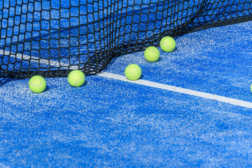 A group of yellow padel balls scattered by the net on a blue court. A Padel Court Detail