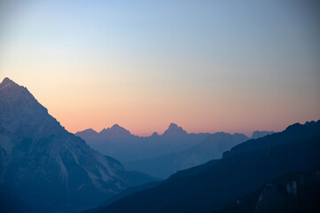 Fototapeta premium Distant mountain peaks layers at sunrise. Pattern of mountains silhouettes against orange sky in Dolomites.