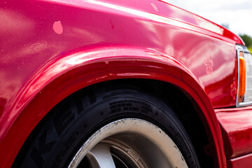 Detailed view of a red car’s fender and tire, showing reflections on the paint and minor surface...