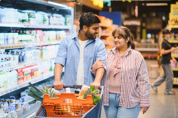 Happy indian couple pushing shopping cart in grocery store