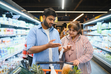 Indian couple discussing groceries in supermarket, choosing products together
