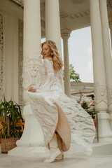  Beautiful slim blonde poses in boho wedding dresses and an embroidered corset on a summer terrace.