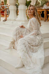  Beautiful slim blonde poses in boho wedding dresses and an embroidered corset on a summer terrace.