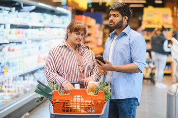 Indian couple using smartphone while shopping for groceries in supermarket